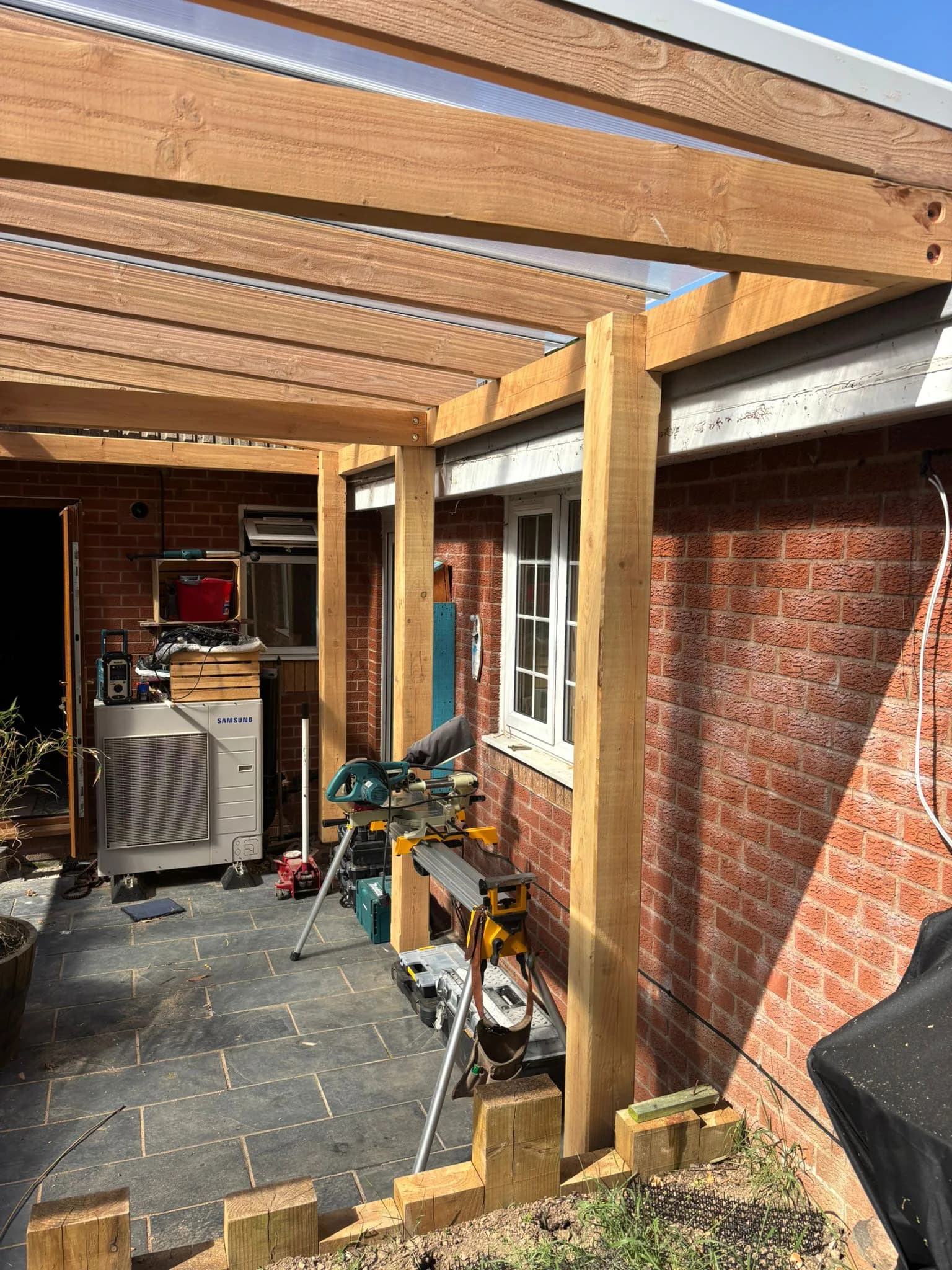 Timber pergola frame being built against a brick house wall