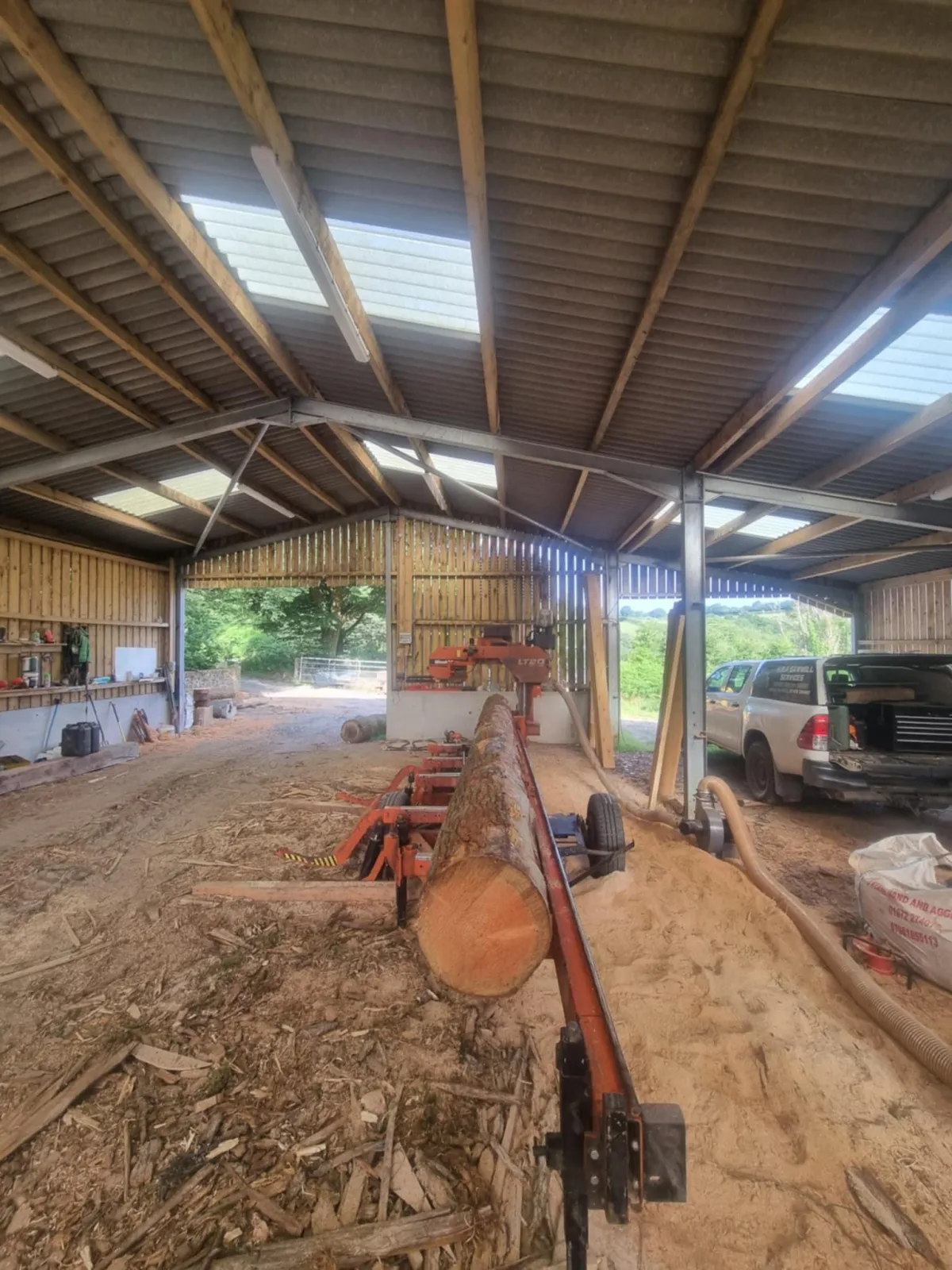 Log being milled on the Woodmizer inside the yard shed, with the yard truck behind